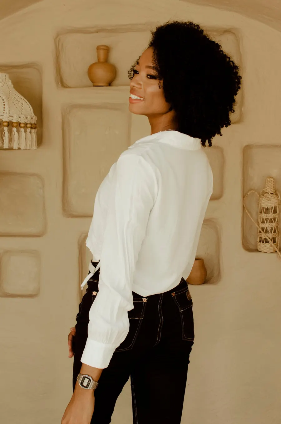 Gabby Faustino de blusa branca, olhando por cima do ombro e sorrindo