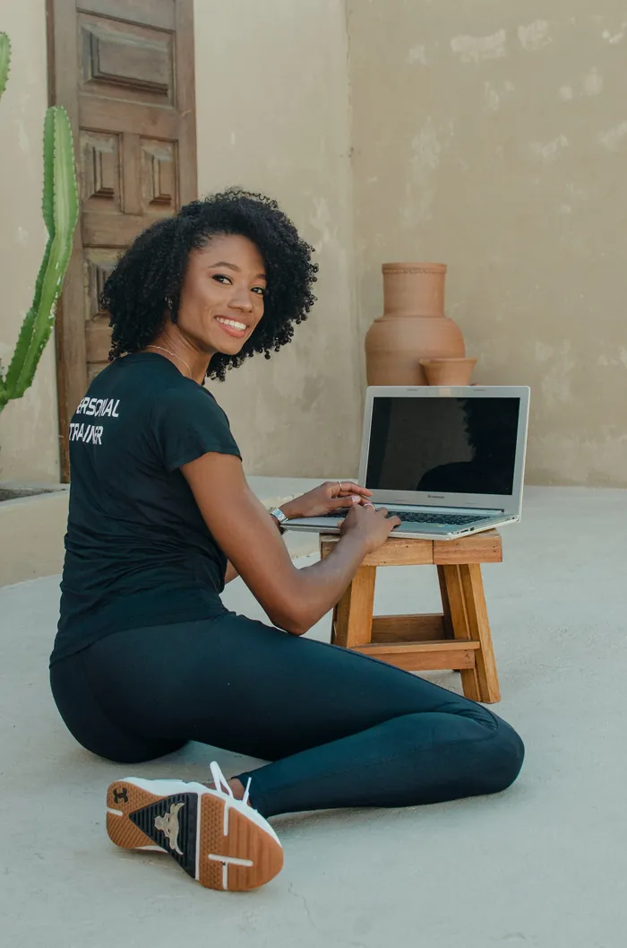 Gabby sentada no chão, sorrindo, digitando em um notebook sobre um banquinho
