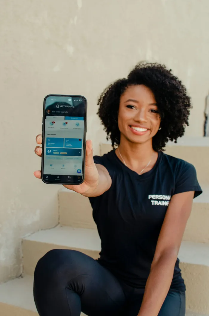 Gabby sorrindo e mostrando na tela do celular o aplicativo dos treinos